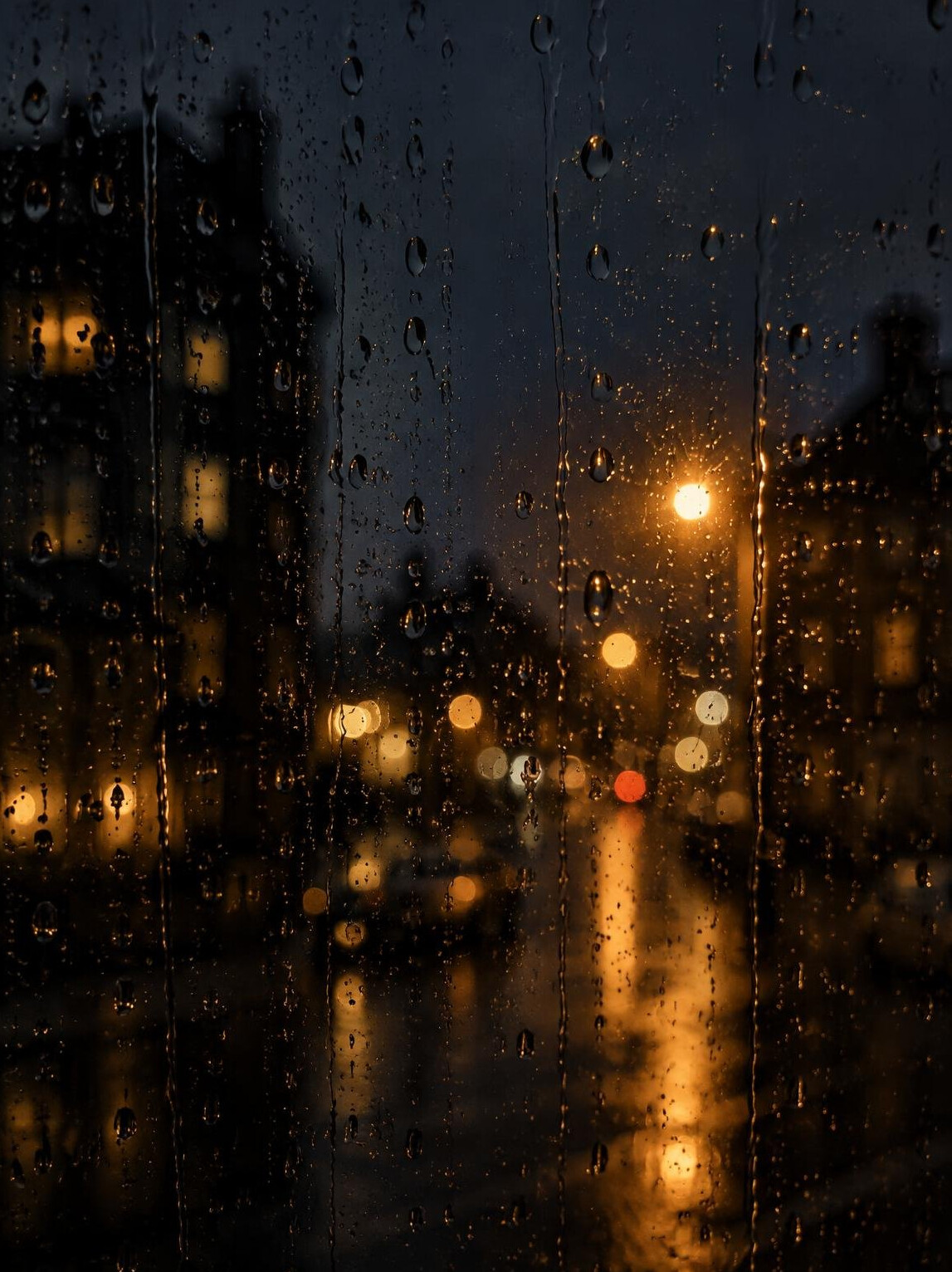 Raindrops on a window with blurred streetlights at night